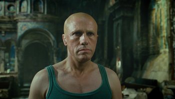 Movie still from “The Zero Theorem” (2013), directed by Terry Gilliam – A bald man in a green tank top; Close Up shot, Low angle
