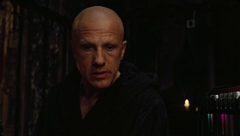 Movie still from “The Zero Theorem” (2013), directed by Terry Gilliam – A man with a bald head is standing in a dark room; Close Up shot, Low angle