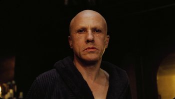 Movie still from “The Zero Theorem” (2013), directed by Terry Gilliam – A man with a bald head wearing a black robe; Close Up shot, Low angle