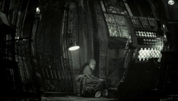 Movie still from “The Zero Theorem” (2013), directed by Terry Gilliam – A person sitting on a chair in a room; Wide shot, Low angle