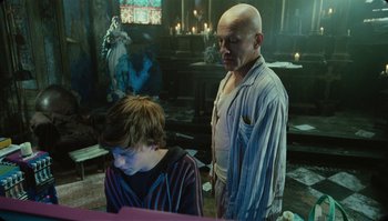 Movie still from “The Zero Theorem” (2013), directed by Terry Gilliam – A man standing next to a young boy in a room; Medium shot, Over the shoulder angle