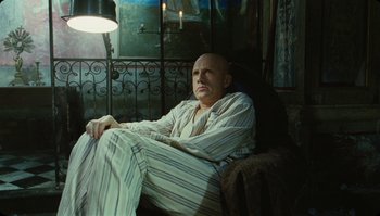 Movie still from “The Zero Theorem” (2013), directed by Terry Gilliam – A bald man sitting in a chair in a room; Medium shot, Low angle