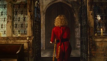 Movie still from “The Zero Theorem” (2013), directed by Terry Gilliam – A woman in a red outfit standing in front of an open door; Wide shot, Over the shoulder angle