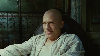 Movie still from “The Zero Theorem” (2013), directed by Terry Gilliam – A bald man sitting in a chair with a white shirt on; Close Up shot, Low angle