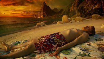 Movie still from “The Zero Theorem” (2013), directed by Terry Gilliam – A man laying on a blanket on the beach; Wide shot, High angle