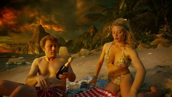 Movie still from “The Zero Theorem” (2013), directed by Terry Gilliam – A man and a woman sitting on the beach with a bottle of champagne; Medium shot, High angle
