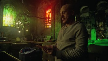 Movie still from “The Zero Theorem” (2013), directed by Terry Gilliam – A bald man is looking at his cell phone in a dark room; Medium shot, Low angle