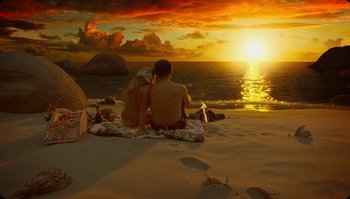 Movie still from “The Zero Theorem” (2013), directed by Terry Gilliam – A man and a woman sitting on the beach at sunset; Extreme Wide shot, High angle