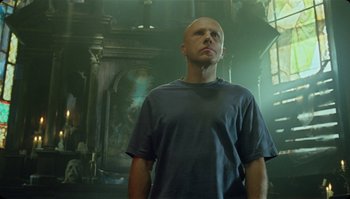 Movie still from “The Zero Theorem” (2013), directed by Terry Gilliam – A man standing in a room with a painting behind him; Medium shot, Low angle