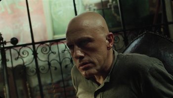 Movie still from “The Zero Theorem” (2013), directed by Terry Gilliam – A man with bald head sitting in front of a window; Close Up shot, Low angle