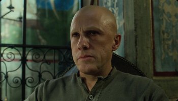 Movie still from “The Zero Theorem” (2013), directed by Terry Gilliam – A man with bald head sitting in a chair looking at the camera; Close Up shot, Low angle