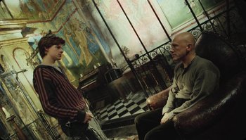 Movie still from “The Zero Theorem” (2013), directed by Terry Gilliam – Two men are sitting in a room talking to each other; Medium shot, Low angle