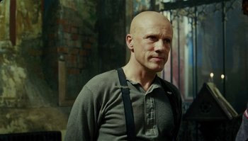 Movie still from “The Zero Theorem” (2013), directed by Terry Gilliam – A bald man wearing a gray shirt and black suspenders; Medium shot, Low angle