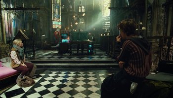 Movie still from “The Zero Theorem” (2013), directed by Terry Gilliam – A man sitting on a tiled floor in front of candles; Wide shot, Over the shoulder angle