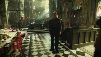 Movie still from “The Zero Theorem” (2013), directed by Terry Gilliam – A man standing inside of a room with black and white checkered floor; Wide shot, High angle