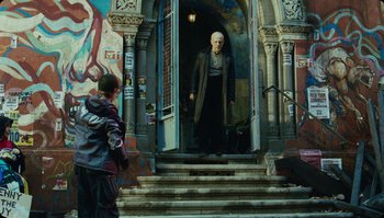 Movie still from “The Zero Theorem” (2013), directed by Terry Gilliam – A man standing in front of an entrance to a building; Wide shot, Low angle