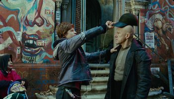 Movie still from “The Zero Theorem” (2013), directed by Terry Gilliam – A man with a hat and a microphone in his ear; Medium shot, Over the shoulder angle
