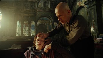 Movie still from “The Zero Theorem” (2013), directed by Terry Gilliam – A bald man is touching the head of a young boy; Medium shot, Low angle