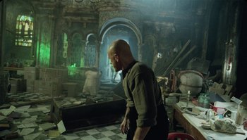 Movie still from “The Zero Theorem” (2013), directed by Terry Gilliam – A man standing in a room filled with lots of stuff; Wide shot, Over the shoulder angle