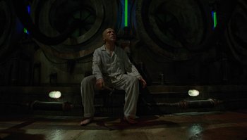 Movie still from “The Zero Theorem” (2013), directed by Terry Gilliam – A man sitting on the ground in front of a wall; Wide shot, Low angle