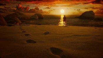 Movie still from “The Zero Theorem” (2013), directed by Terry Gilliam – A man standing on a beach watching the sun go down over the ocean; Extreme Wide shot, High angle