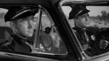 Movie still from “Them!” (1954), directed by Gordon Douglas – Two police officers in a car looking in the mirror; Medium shot, Low angle