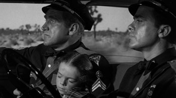 Movie still from “Them!” (1954), directed by Gordon Douglas – A black and white photo of a police officer and two other people in a car; Medium shot, Over the shoulder angle