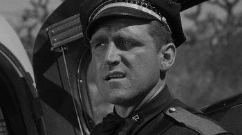 Movie still from “Them!” (1954), directed by Gordon Douglas – A man in a uniform holding an umbrella in front of a building; Close Up shot, Low angle
