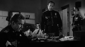 Movie still from “Them!” (1954), directed by Gordon Douglas – A black and white photo of a man standing in front of other men; Medium shot, Low angle