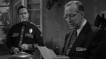 Movie still from “Them!” (1954), directed by Gordon Douglas – A man in glasses is reading a piece of paper next to another man in a uniform; Medium shot, Over the shoulder angle