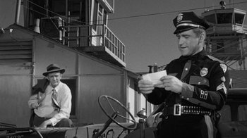 Movie still from “Them!” (1954), directed by Gordon Douglas – A police officer holding papers while sitting in a car; Medium shot, Over the shoulder angle