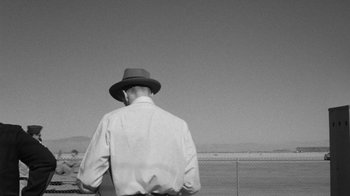 Movie still from “Them!” (1954), directed by Gordon Douglas – A man wearing a hat is looking over a fence; Wide shot, Over the shoulder angle
