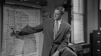 Movie still from “Them!” (1954), directed by Gordon Douglas – A black and white photo of a man in a suit pointing to a map; Medium shot, Low angle