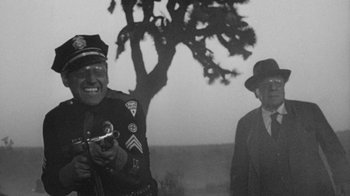 Movie still from “Them!” (1954), directed by Gordon Douglas – Two men standing next to each other in front of a tree; Medium shot, Over the shoulder angle