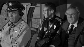 Movie still from “Them!” (1954), directed by Gordon Douglas – A police officer sitting in a helicopter next to two other officers; Medium shot, Over the shoulder angle