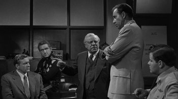 Movie still from “Them!” (1954), directed by Gordon Douglas – A group of men standing next to each other in a room; Medium shot, Over the shoulder angle