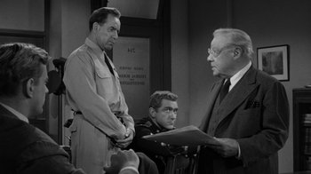 Movie still from “Them!” (1954), directed by Gordon Douglas – Three men are standing in front of each other; Medium shot, Over the shoulder angle