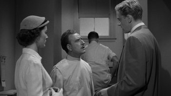 Movie still from “Them!” (1954), directed by Gordon Douglas – A group of people standing around talking to each other in a room; Medium shot, Over the shoulder angle