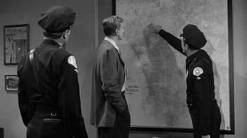 Movie still from “Them!” (1954), directed by Gordon Douglas – A group of men standing next to each other near a map; Medium shot, Over the shoulder angle