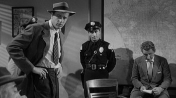 Movie still from “Them!” (1954), directed by Gordon Douglas – A police officer standing next to a man in front of a chair; Medium shot, Over the shoulder angle