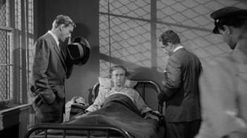 Movie still from “Them!” (1954), directed by Gordon Douglas – Three men in suits and hats standing next to a man in a hospital bed; Medium shot, High angle