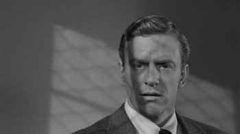 Movie still from “Them!” (1954), directed by Gordon Douglas – Black and white photograph of a man wearing a suit and tie; Close Up shot, Over the shoulder angle