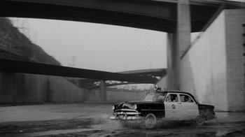 Movie still from “Them!” (1954), directed by Gordon Douglas – An old police car driving down a street; Wide shot, Low angle