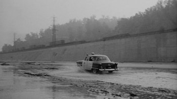 Movie still from “Them!” (1954), directed by Gordon Douglas – An old police car driving down a flooded road; Extreme Wide shot, High angle