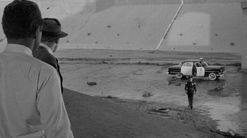 Movie still from “Them!” (1954), directed by Gordon Douglas – A man standing on a dirt field next to a white car; Extreme Wide shot, High angle