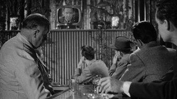 Movie still from “Them!” (1954), directed by Gordon Douglas – A group of people sitting at a bar watching a television; Medium shot, Over the shoulder angle