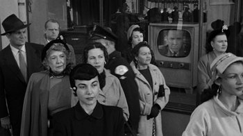 Movie still from “Them!” (1954), directed by Gordon Douglas – Black and white photograph of a group of people watching television; Medium shot, Over the shoulder angle
