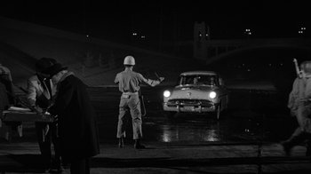 Movie still from “Them!” (1954), directed by Gordon Douglas – A man in a white helmet standing in front of a car; Wide shot, Over the shoulder angle