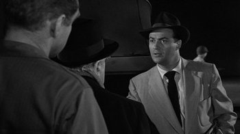 Movie still from “Them!” (1954), directed by Gordon Douglas – A black and white photo of a man in a suit and a hat; Close Up shot, Over the shoulder angle
