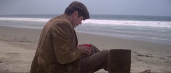 Movie still from “They Shoot Horses, Don't They?” (1969), directed by Sydney Pollack – A man sitting on the beach holding a red object; Wide shot, High angle